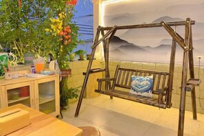 A wooden swing with cushions, a wooden table, and a cabinet with items on it. - Alley See You Inn (Danxia Mountain Scenic Area) (Renhua)