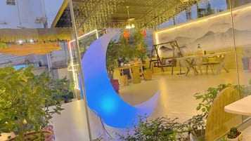 A restaurant with a large illuminated crescent moon decoration, indoor plants, and a mountain mural on the wall.