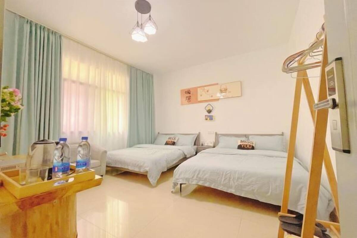 A hotel room with two beds, a wooden desk with water bottles, a ladder, and a wall-mounted TV.
