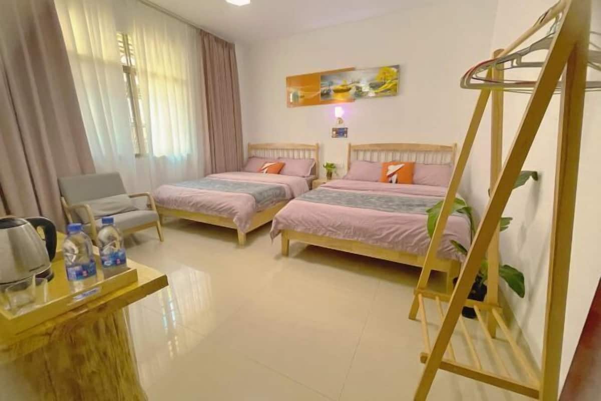 A hotel room with two beds, a desk with a kettle and water bottles, a chair, and a ladder against the wall.