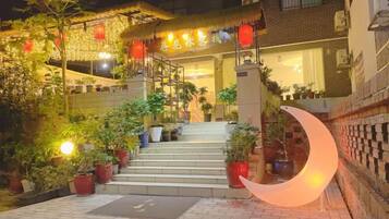 A hotel entrance with steps leading up to a building, potted plants, and a crescent-shaped light fixture.