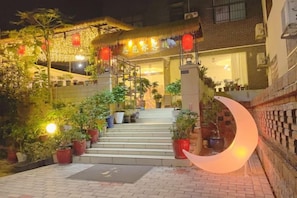 A hotel entrance with steps leading up to a building, potted plants, and a crescent-shaped light fixture.