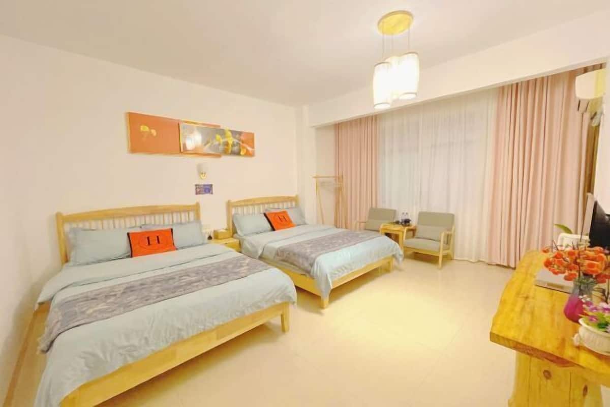 A hotel room with two beds, a desk, a chair, and a large window with curtains.