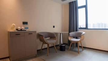 Habitación de hotel moderna con un aparador de madera, dos sillas grises, una mesita redonda y una ventana con vistas a edificios.