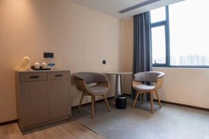 Habitación de hotel moderna con un aparador de madera, dos sillas grises, una mesita redonda y una ventana con vistas a edificios.