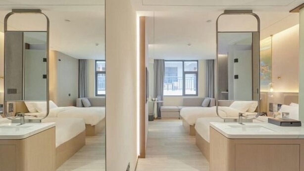 Habitación de hotel con dos camas, un espejo grande, un baño con lavamanos y vistas a la ciudad.