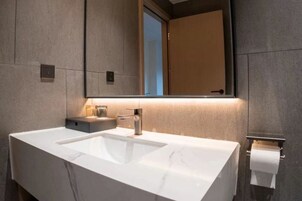 Un baño moderno con un lavamanos blanco grande, un espejo y un dispensador de papel higiénico.
