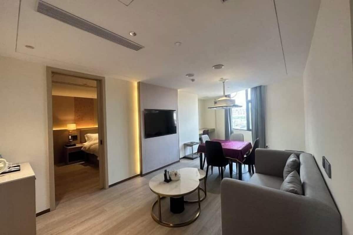 A modern hotel room with a dining area, a sofa, a TV, and a bed.