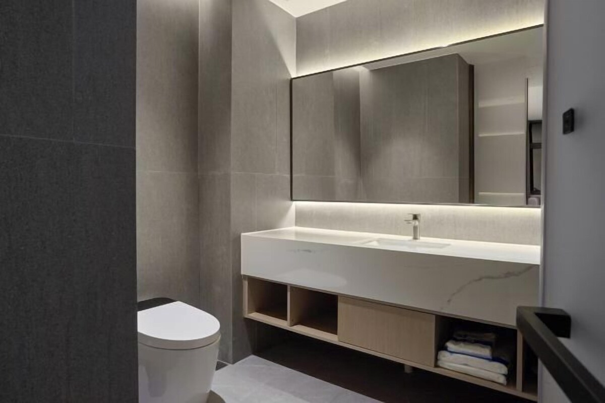 Un baño moderno con un espejo grande, lavamanos blanco y estantes integrados.
