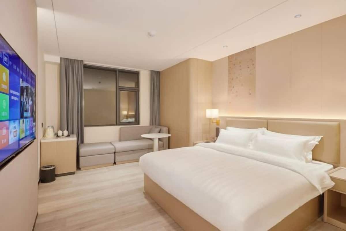 A hotel room with a bed, a TV, a sofa, a small table, and a window with curtains.