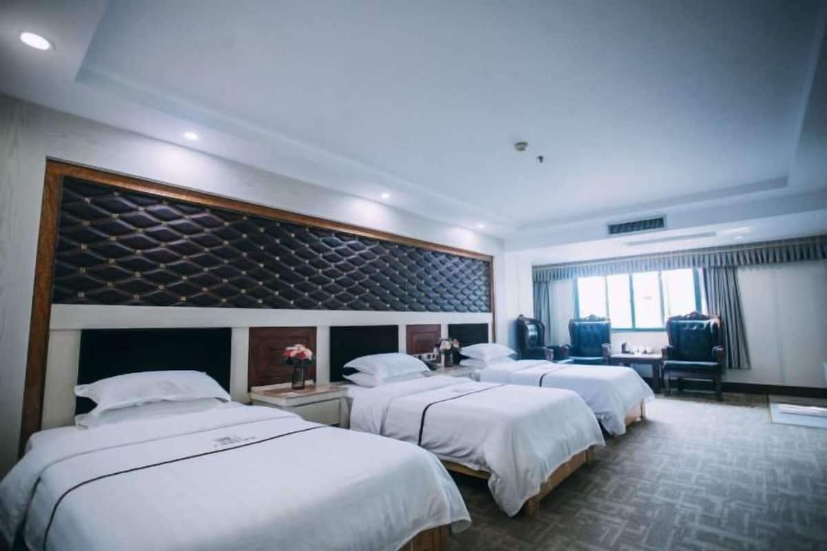 A hotel room with three beds, a large padded headboard, a desk, and a chair.