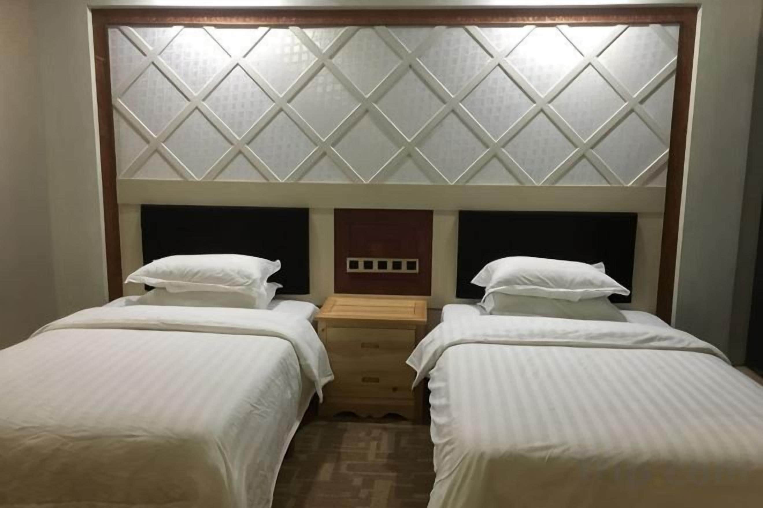 A hotel room with two single beds, a wooden nightstand, and a headboard with a diamond-patterned design.