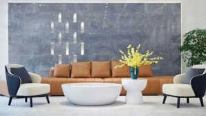 Una sala de estar moderna con un sofá de cuero marrón, dos sillones, una mesa de centro blanca y un jarrón con flores amarillas.