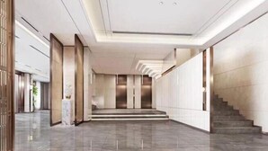 Un vestíbulo moderno con piso de mármol, una escalera y una recepción con ascensores.