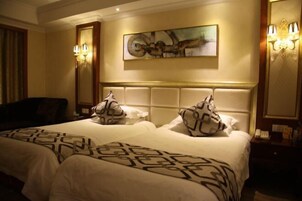 Quarto de hotel com duas camas, uma pintura abstrata grande e arandelas.