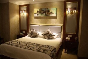 Habitació d'hotel amb un llit gran, dues taules de nit, un quadre a la paret i dues làmpades penjades a la pared.