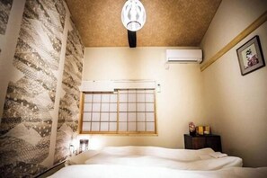 Ein Zimmer mit einem Bett, einem Fenster mit Gittermuster, einer Klimaanlage und einer Wandleuchte.