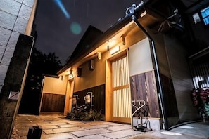 A house with a garage door, a wooden fence, and a stone pathway leading to the entrance. - Kyomachiya Miss (Kyoto)