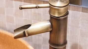 A brass faucet with a modern design, mounted on a wall with a tiled backsplash.