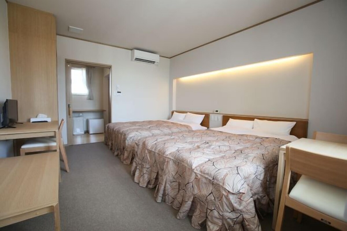 Een hotelkamer met een tweepersoonsbed, een bureau met stoel, een kitchenette en een badkamer zichtbaar door een geopende deur.