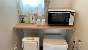 Een compacte kitchenette met een magnetron, een kleine koelkast en een waterkoker op een houten aanrecht.
