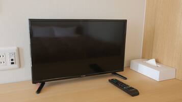 A flat-screen TV on a wooden desk with a remote control and a tissue box.