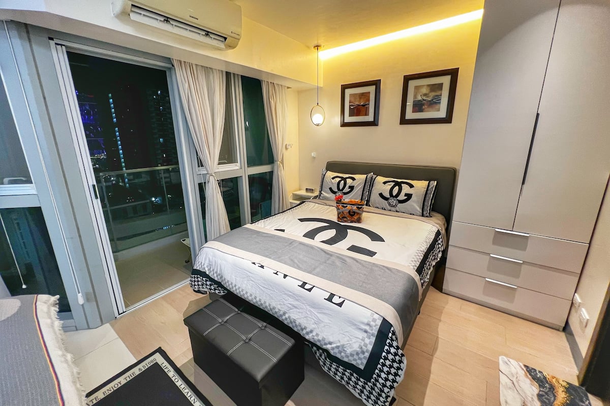 A modern bedroom with a large bed, a wardrobe, and a sliding glass door leading to a balcony.