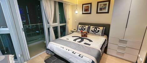 A modern bedroom with a large bed, a wardrobe, and a sliding glass door leading to a balcony.