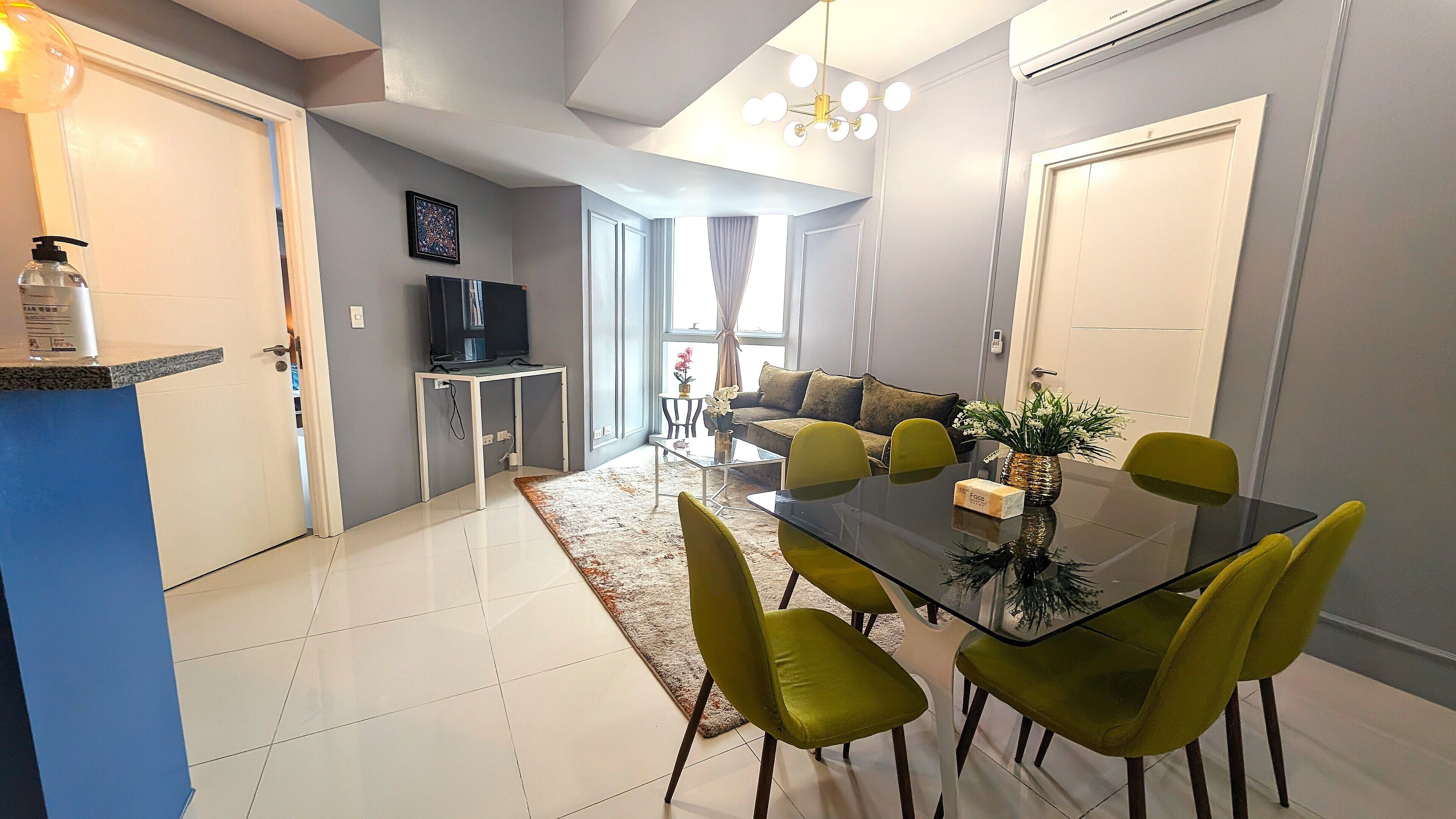 Ein modernes Wohnzimmer mit einem Glastisch, grünen Stühlen, einer Couch und einem Fernseher.