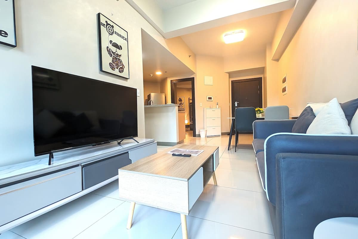 A modern living room with a flat-screen TV, a sofa, a coffee table, and a dining area in the background.