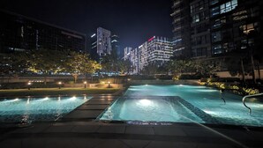 Vue nocturne d’une piscine sur le toit, avec des bâtiments modernes en arrière-plan.