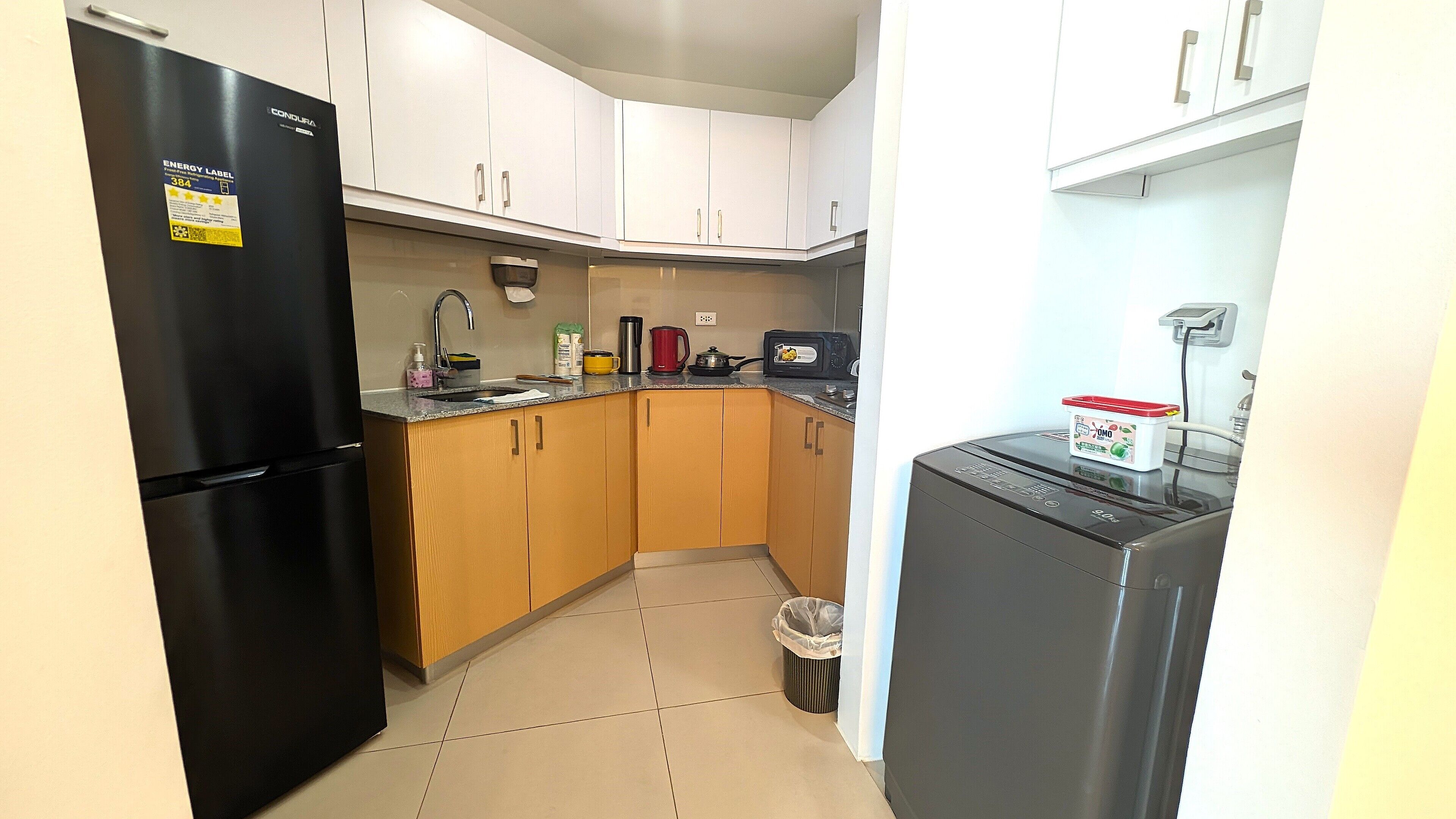 A compact kitchen with white cabinets, a black refrigerator, a microwave, and a small trash bin.
