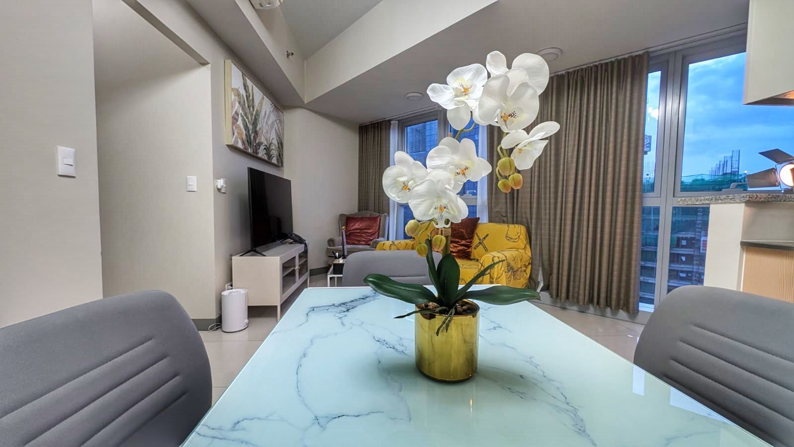 Een moderne woonkamer met een marmeren tafel, een potorkidee en een gele fauteuil.