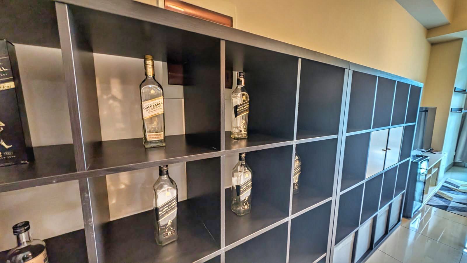 Un hall d’hôtel moderne avec un sol carrelé en noir et blanc, une vitrine en verre contenant diverses bouteilles d’alcool et un escalier menant à un autre niveau.