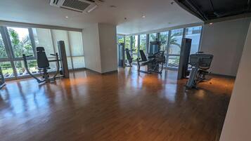 A spacious gym with large windows, wooden flooring, and various exercise machines.
