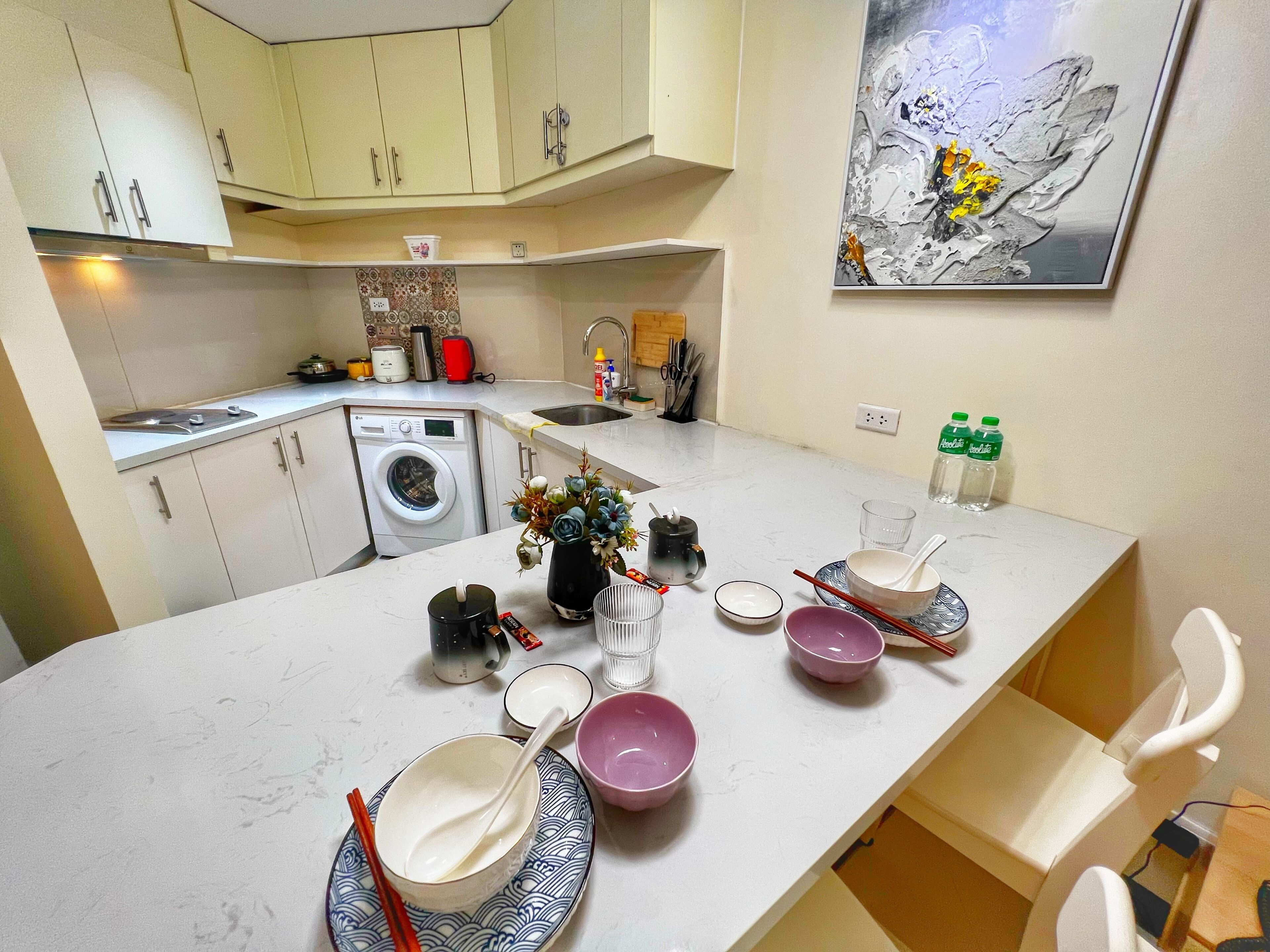 A compact kitchen with a washing machine, a sink, and a dining area with bowls and chopsticks.