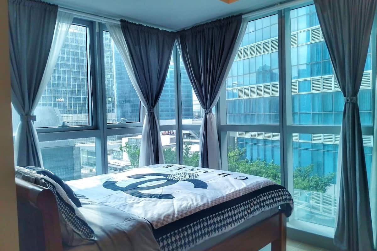 A bedroom with a large window, a bed with a patterned bedspread, and curtains.