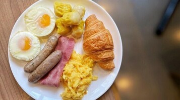 A plate with scrambled eggs, sausages, ham, a croissant, and two fried eggs.