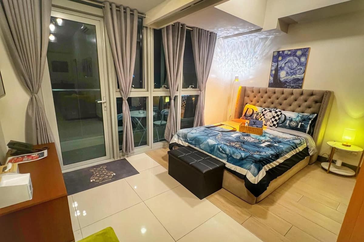 A modern bedroom with a large bed, a tufted headboard, and a view through the sliding glass door.