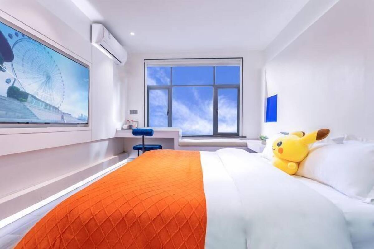 A modern hotel room with a large bed, a desk, and a window with a view of a Ferris wheel.