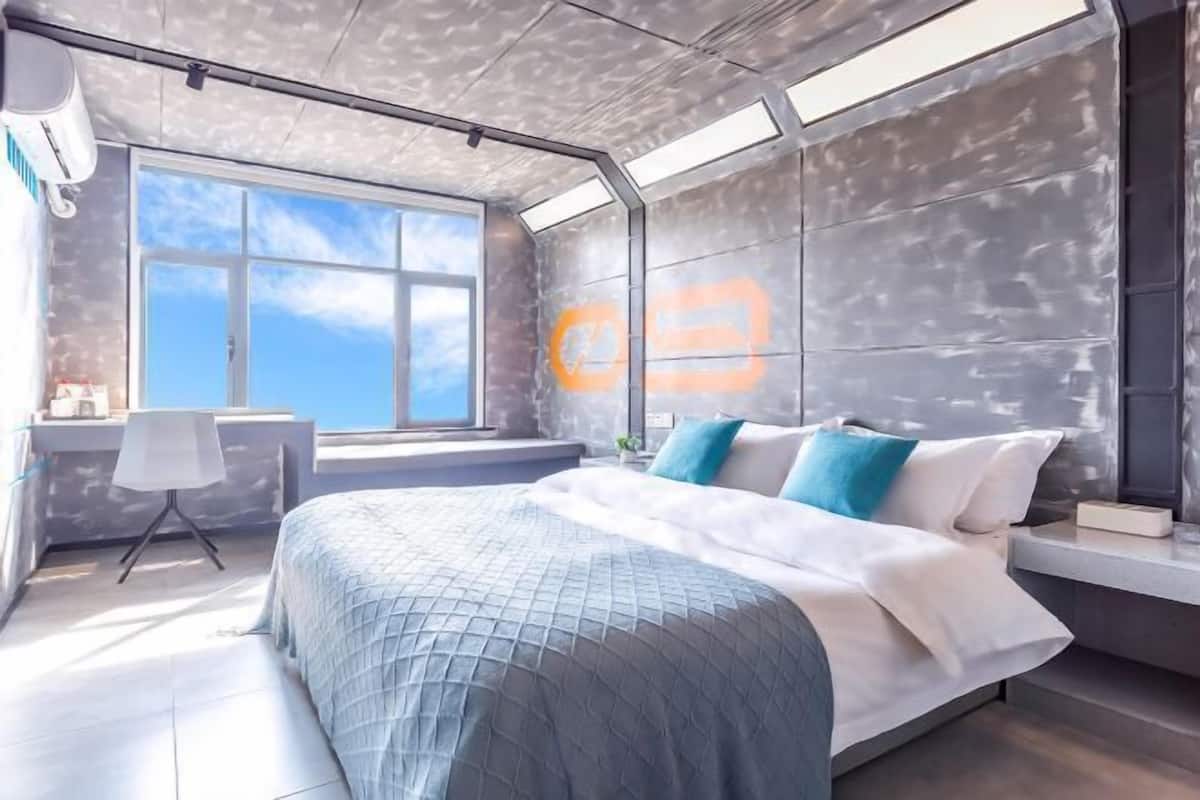 A modern bedroom with a large bed, a desk, and a window with a view.