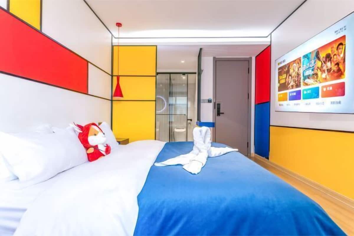 A hotel room with a bed, a red hanging light, a glass door, and a wall with movie posters.