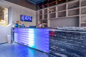 A reception area with a marble counter, a television screen, and shelves with decorative items. - Xinzheng Xuanjuzi Hotel (Xias International College) (Xinzheng)