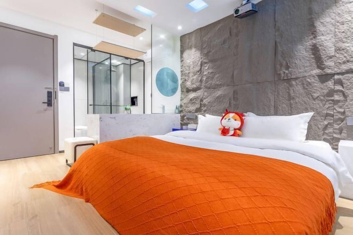 A modern hotel room with a large bed, a stone accent wall, a white headboard, and a large mirror.