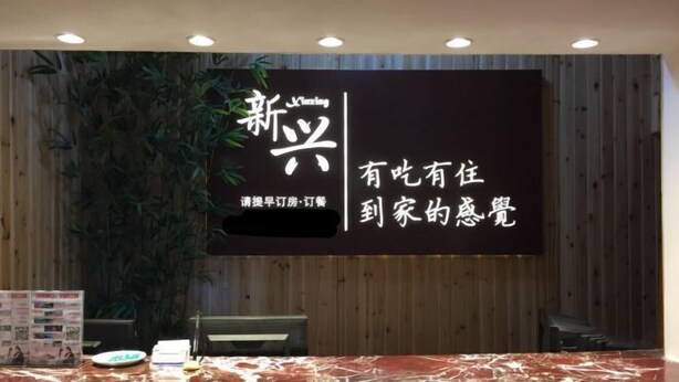 A reception desk with a wooden backdrop and a large illuminated sign. - Shipu Xinxing Hotel (Xiangshan)