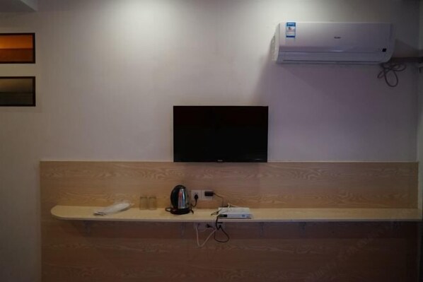 A reception area with a flat-screen TV mounted on the wall, a coffee machine, and a power strip on a wooden counter. - Shipu Xinxing Hotel (Xiangshan)