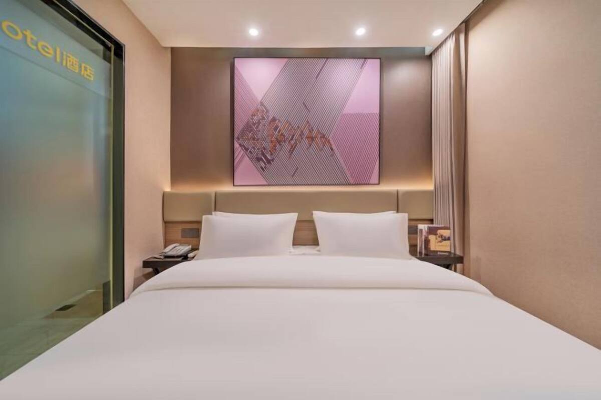 Une chambre d’hôtel moderne avec un grand lit, une œuvre d’art accrochée au mur et une porte en verre avec une pancarte.