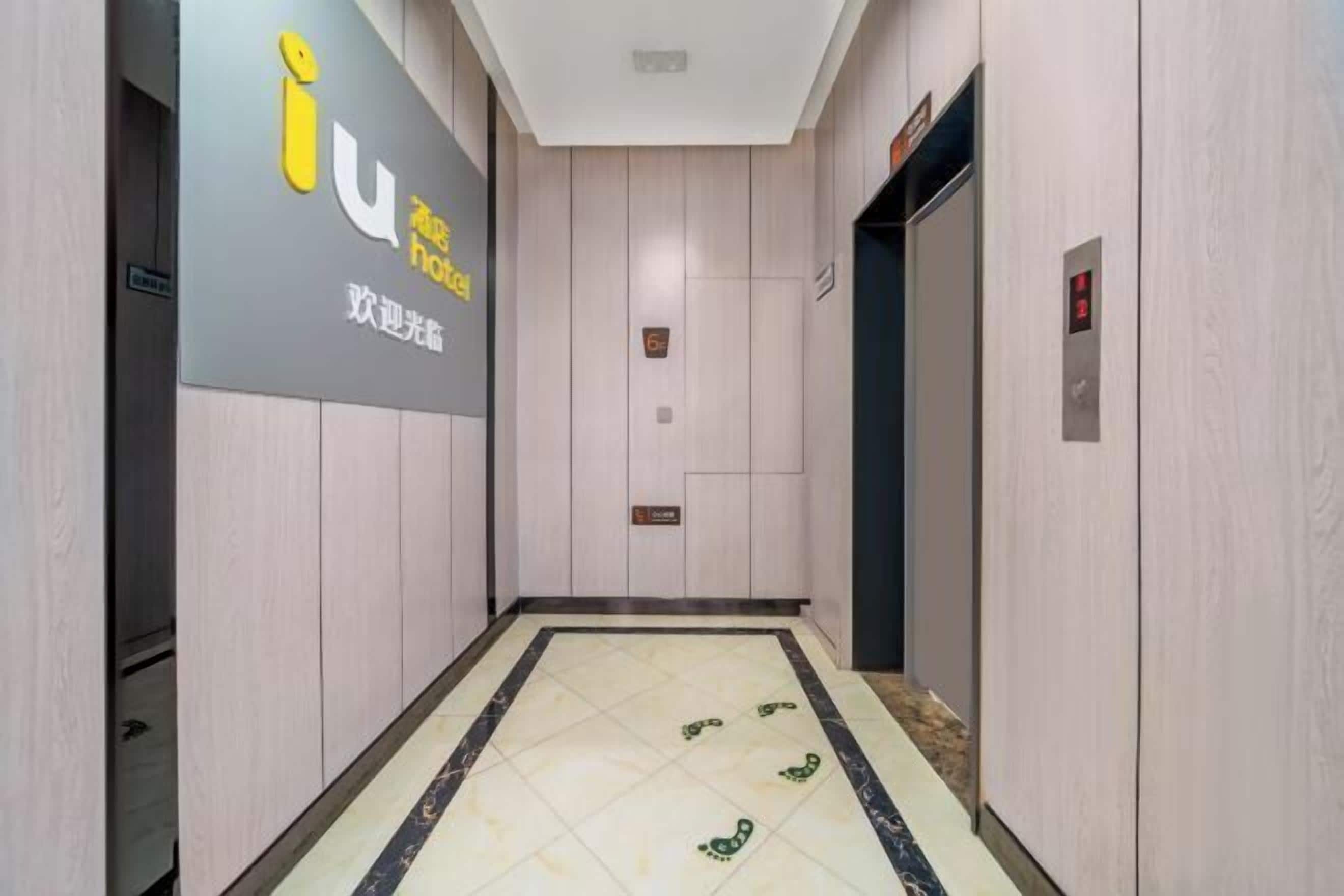 A hotel corridor with a tiled floor, a sign with the hotel's logo, and an elevator.