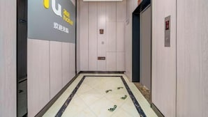 Een hotelgang met een betegelde vloer, een bord met het logo van het hotel en een lift.