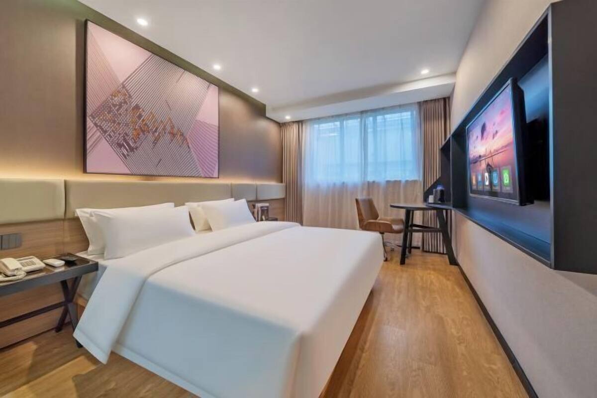 Une chambre d’hôtel avec un grand lit, un bureau avec un téléphone, un téléviseur fixé au mur et une fenêtre avec des rideaux.